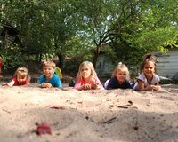 Kinder liegen nebeneinander im Sand