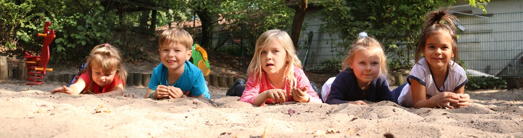 Kinder liegen nebeneinander auf dem Bauch im Sand